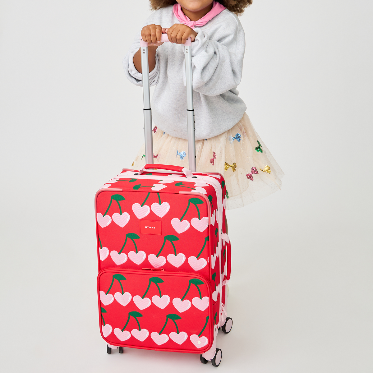 girl pushing STATE Bags Logan Carry-On Suitcase Cherry