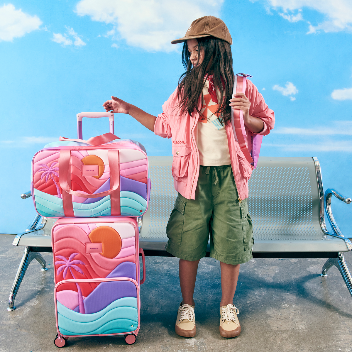 Girl sitting at airport with state bags rockaway duffle sunset and logan carry-on sunset